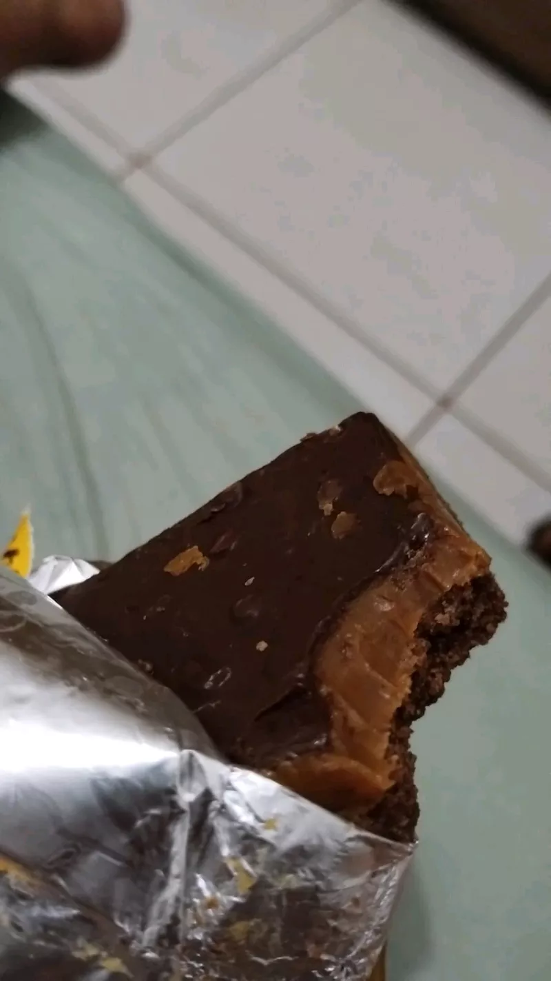 Unidade da torta sendo retirada da embalagem de alumínio, focando no brilho da cobertura de chocolate