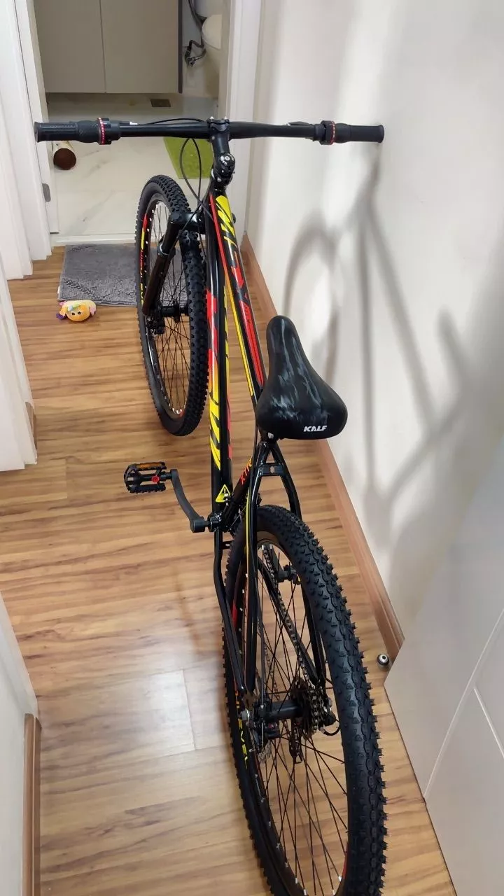 Bicicleta MTB KGT apoiada em parede interna, quadro preto e detalhes em verde, com aro 29 e pneus para terrenos irregulares