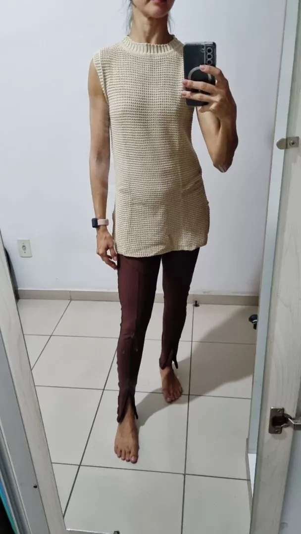 Mulher usando colete de tricô bege com calça marrom de barra dobrada.