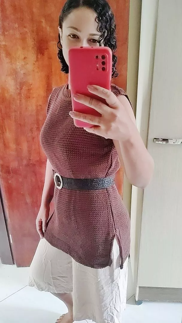 Mulher usando colete de tricô marrom acinturado com cinto preto e calça clara.