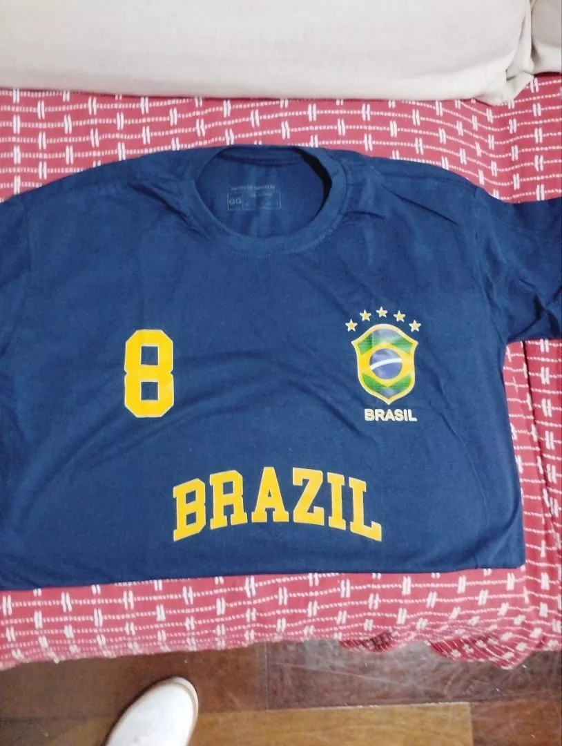 Camiseta feminina azul marinho com estampa do Brasil e número 8 dobrada sobre colcha vermelha xadrez