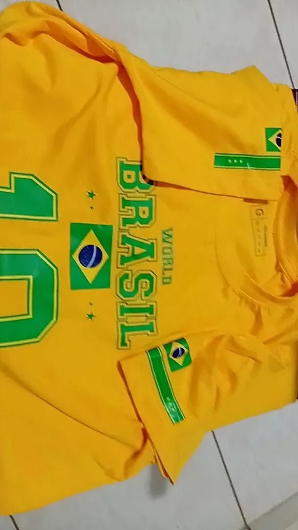 Vista superior da camisa do Brasil amarela estendida no chão, mostrando detalhes da gola e mangas com bandeiras
