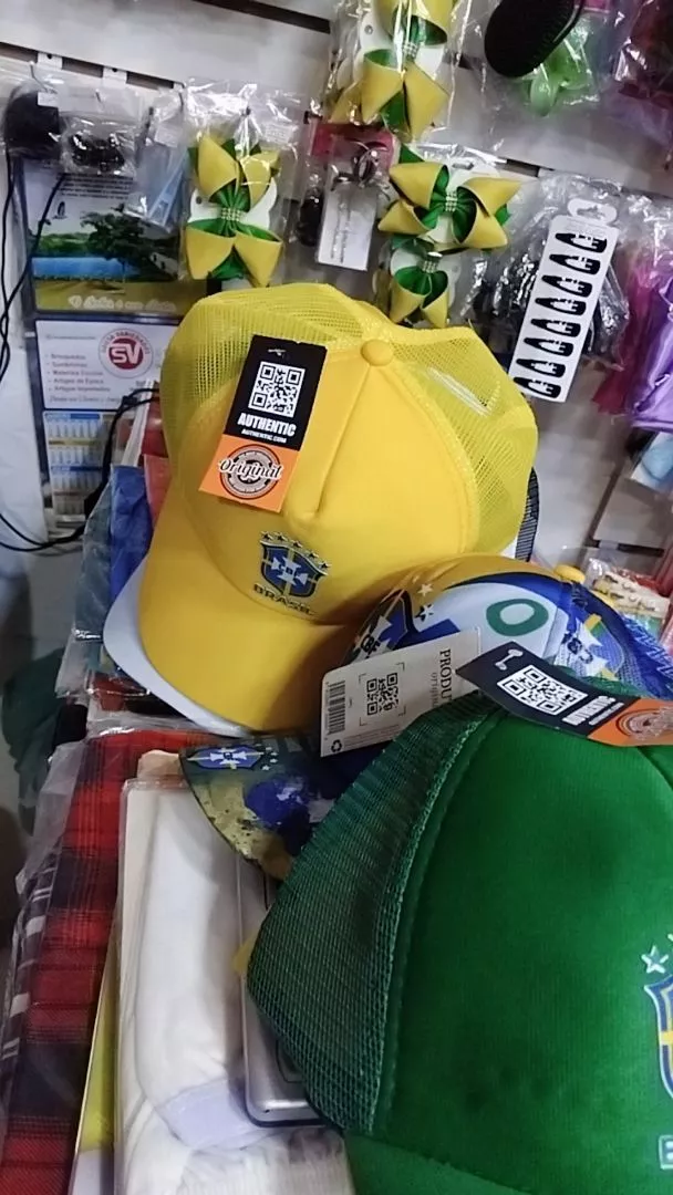 Close em boné amarelo do Brasil com etiqueta de autenticidade pendurada e outros bonés ao fundo em ambiente de loja
