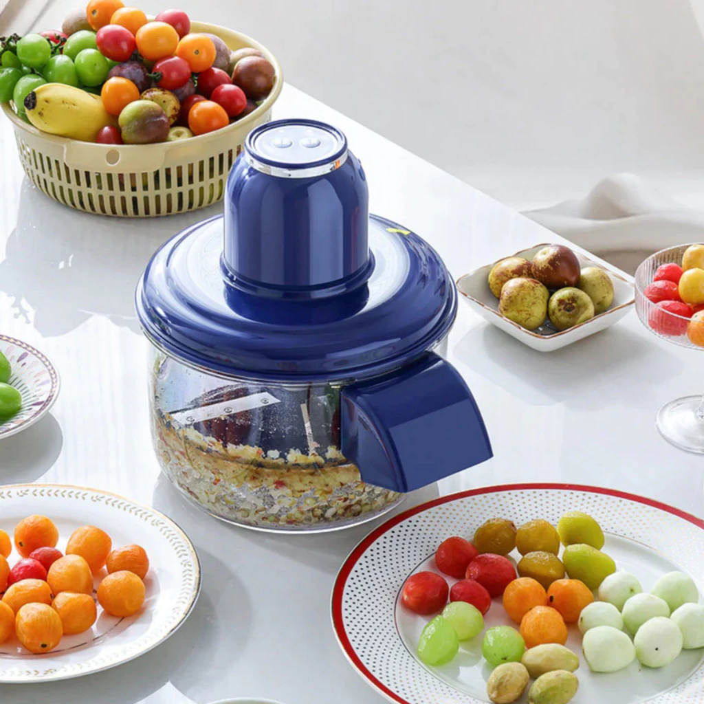 Visão superior do descascador elétrico em uso sobre uma mesa com variadas frutas coloridas e pratos.