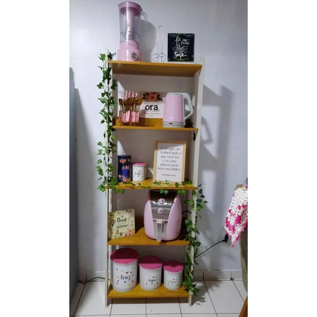 Estante estilo industrial de madeira e metal branco decorada com eletrodomésticos cor-de-rosa e plantas artificiais.