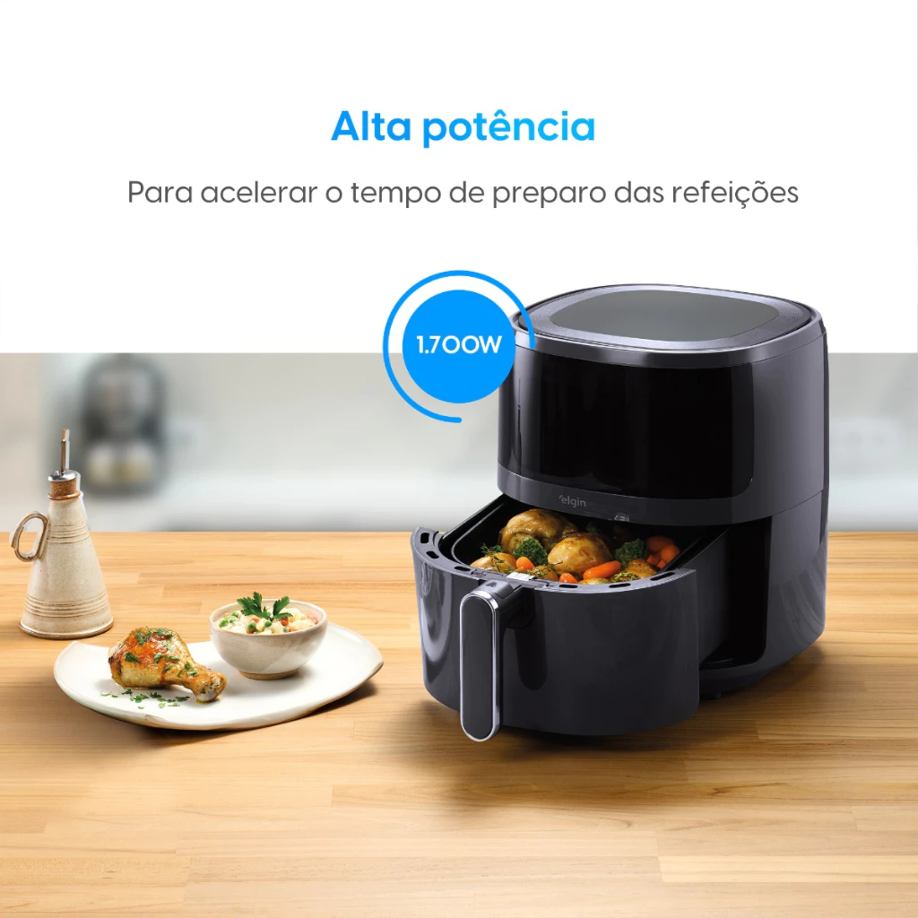 Fritadeira Elgin Visio Fry cinza escura com o cesto aberto contendo vegetais assados, em uma cena de cozinha com um prato de frango e salada.