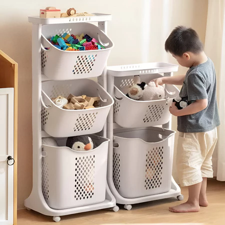 Menino de pé ao lado de um organizador de brinquedos branco com rodas, com cestas cheias de brinquedos.
