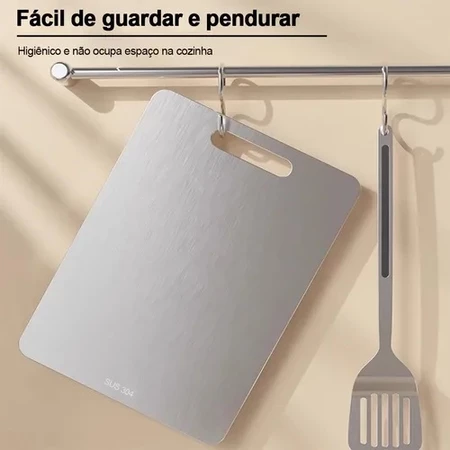 Tábua de corte em aço inoxidável pendurada em um suporte de parede de cozinha ao lado de uma espátula de metal.