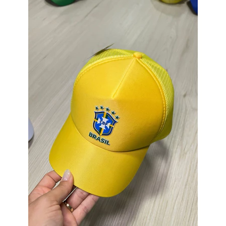 Boné amarelo do Brasil com tela traseira e escudo da CBF bordado, segurado por uma mão