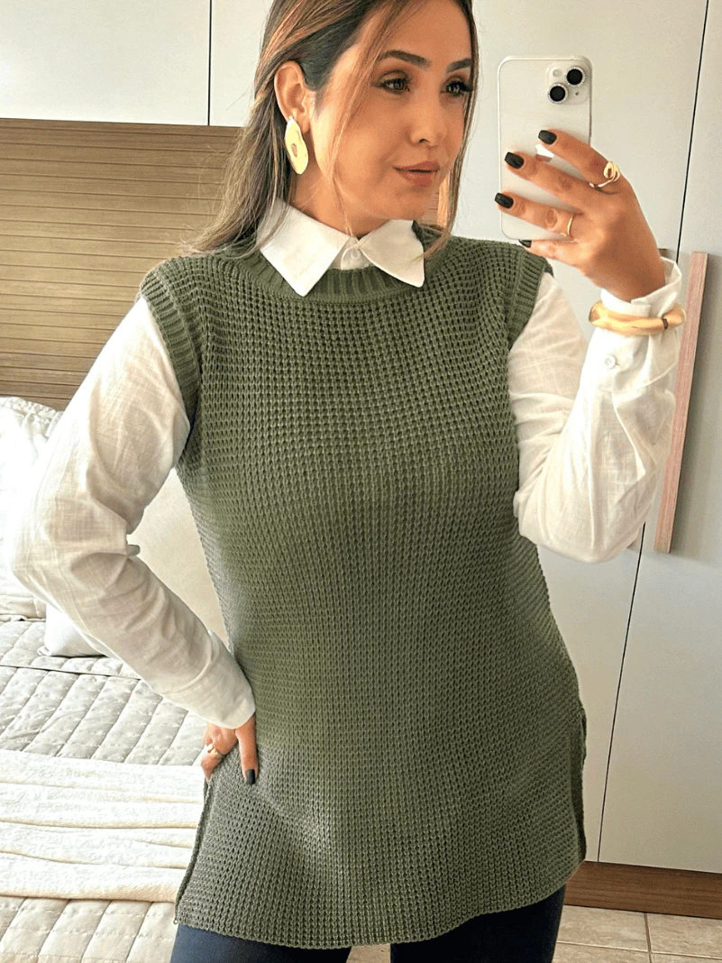 Mulher usando colete de tricô verde musgo sobre camisa branca, com calça preta.