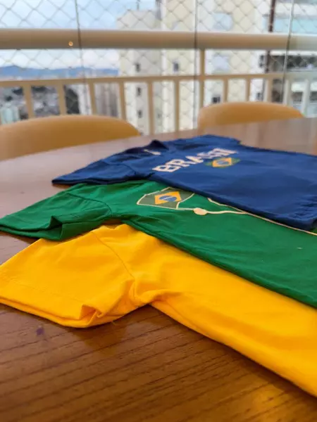 Três camisas dobradas, azul, verde e amarela, sobre uma mesa com vista para a cidade.