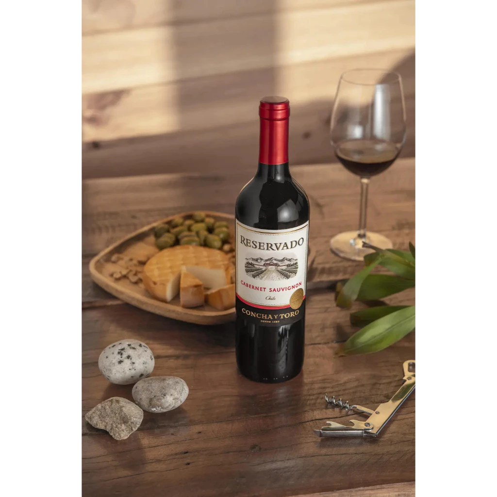 Garrafa de vinho Reservado Cabernet Sauvignon em uma mesa de madeira com taça e petiscos
