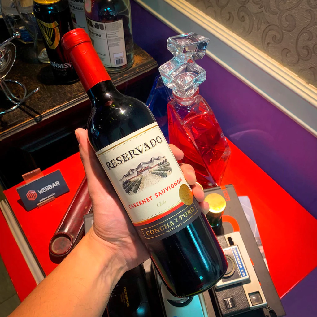 Mão segurando uma garrafa de vinho Reservado Cabernet Sauvignon em ambiente decorado
