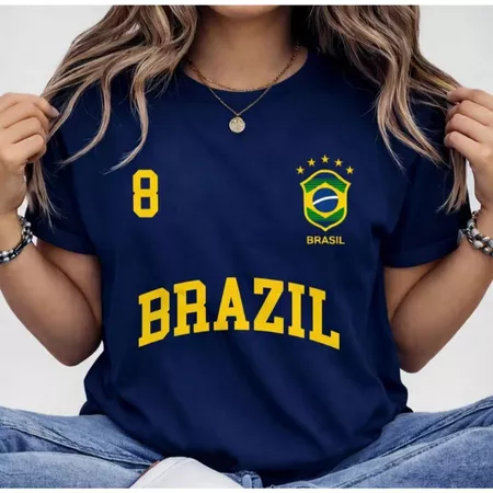 Modelo vestindo camiseta azul marinho com estampa amarela do Brasil e número 8, acessórios dourados e calça jeans
