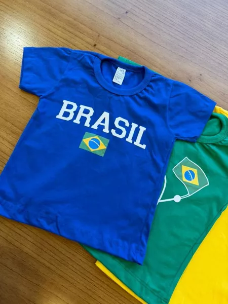 Camisa azul BRASIL e detalhes de verde e amarelo em uma mesa de madeira.