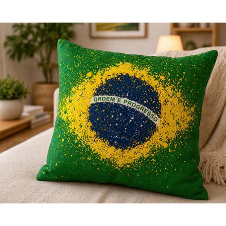 Close em uma capa de almofada verde com estampa do mapa do Brasil e a frase Ordem e Progresso em estilo respingado.