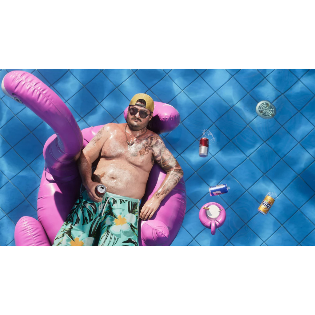 Vista aérea de um homem com tatuagens, usando boné amarelo e shorts floridos, relaxando em uma boia de flamingo rosa em uma piscina azul, com latas de bebida flutuando ao redor.