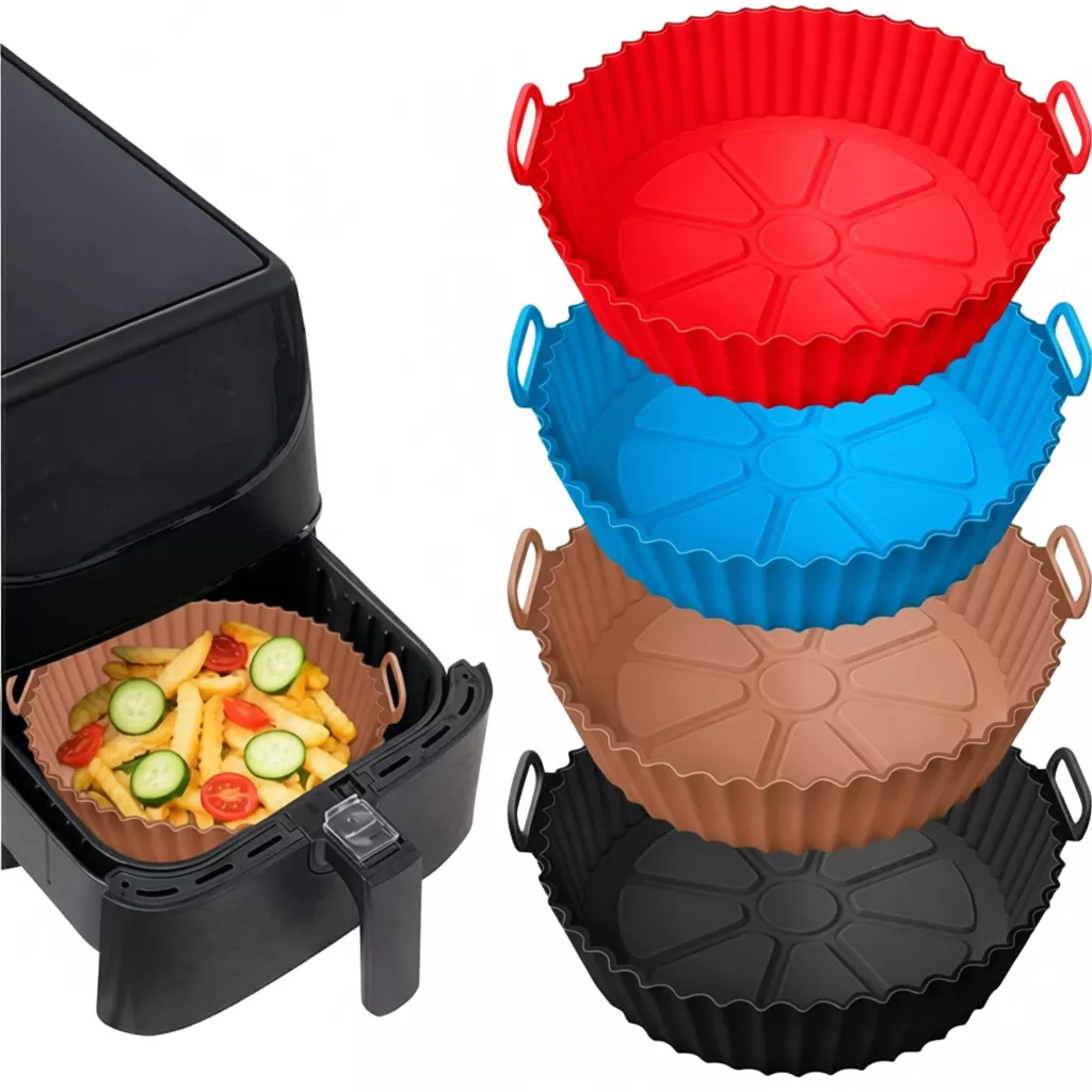 Montagem de fotos mostrando formas de silicone reutilizáveis para Air Fryer. À esquerda, uma Air Fryer preta com a gaveta aberta contendo uma forma marrom com batatas fritas e rodelas de pepino e tomate. À direita, uma pilha vertical de quatro formas de silicone nas cores vermelha, azul, marrom e preta. As formas possuem laterais onduladas e pequenas alças laterais.